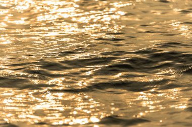Su yüzeyi hareket eden altın su dalgalarıyla yansıyor.