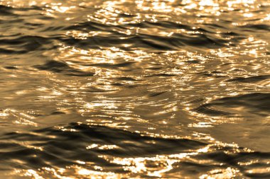 Su yüzeyi hareket eden altın su dalgalarıyla yansıyor.