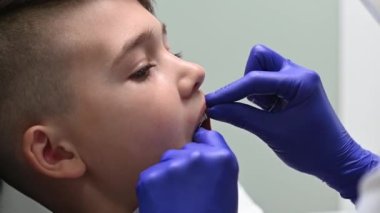 Diş hekimi bir çocuğun dişlerini diş ipiyle fırçalıyor.