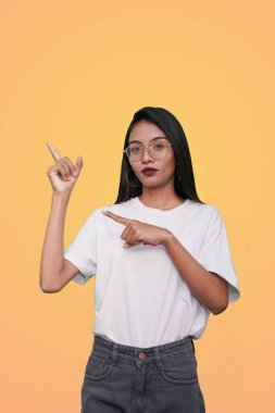 Beyaz tişörtlü, turuncu arka planda genç Asyalı kadın sol tarafını işaret ediyor..