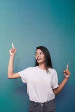 Genç Asyalı kadın beyaz tişört giyiyor mavi arka planda kendini işaret ediyor..