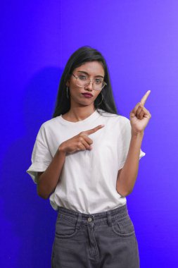 Kafası karışmış genç bir kadın kaşlarını çatıyor, yargılıyor, sırıtıyor ve üzgün ve hoşnutsuz görünüyor, sağ üst köşeyi işaret ediyor. Reklam kavramı.