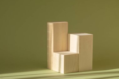 Güneş ışığı altında yeşil zemin üzerinde ahşaptan yapılmış kare tribünleri oluşturun. Kozmetik ürünlerin sunumu ve ürünlerin tanıtımı için Geometrik 3d podyumu.