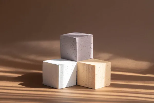 3d podium, for presentations of packaging, cosmetics. Three cubes of different colors, beige, white, brown, arranged in form of pedestal in rays of sunlight.