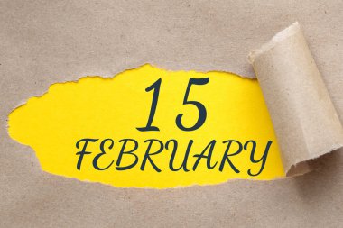 15 Şubat. Ayın 15. günü, takvim tarihi. Kenarları yırtılmış kağıt delikleri. Sarı arkaplan yırtık pırtık delikten görülebilir. Kış ayı, yılın günü konsepti..