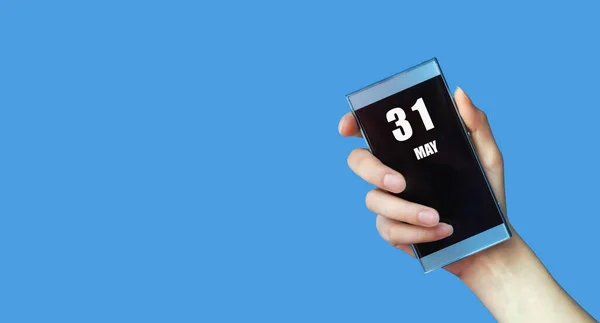 31 Mayıs. Ayın 31 'i, takvim tarihi. Mavi izole edilmiş arka planda boş ekranı olan bir kadının eli cep telefonunu tutuyor. Bahar ayı, yılın günü konsepti..