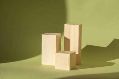 Üç boyutlu podyum kavramı. Ahşap, yeşil zemin üzerinde çeşitli kare şekilli güneş ışınları altında duruyor. Nesnelerin sert gölgesi duvar kağıdının yüzeyine düşer. Güzellik reklamı için model.