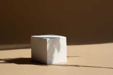 Paketleme ve kozmetik sunumları için 3D podyum kavramı. Beyaz polistirenden yapılmış küp, güneş ışığı ışınlarıyla kahverengi arkaplana gölge düşürür.