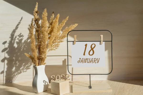 january 18. 18th day of month, calendar date. White vase with dead wood next to the numbers 2022 and stand with an empty sheet of paper on table. Concept of day of year, time planner, winter month.