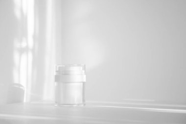 Kozmetik ürünlerini güneş ışığında paketlemek için beyaz plastik kavanoz. Yakın plan, tek renkli arka plan. Güzellik endüstrisi kavramı.
