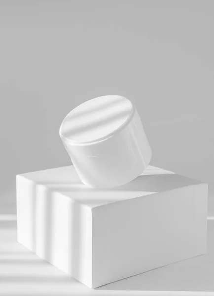 Κενό λευκό βάζο με κρέμα στο τετράγωνο σταθεί στο φως του ήλιου. Λευκό απομονωμένο φόντο με σκιές. Κρεμαστό προϊόν για καλλυντικά συσκευασίας, πάνω από 3d βάθρο. Κάθετη εικόνα, κοντινό πλάνο — Φωτογραφία Αρχείου