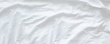 Beyaz buruşuk fabik doku geniş bir zemin oluşturmuş yatak odasındaki yapılmamış yatak çarşaflarını kapatmış.