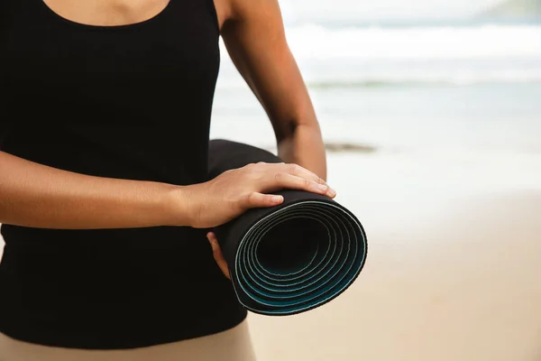 Woman in sport suite carry yoga mattress on the beach,Sport background.healthy lifestyle and travel. Sport female equipment.