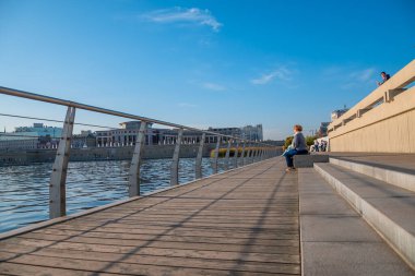 Kazan, Rusya - 14 Ekim 2020: Ahşap yaya yolu ve metal çitli şehir gölü seti. Vatandaşlar gün batımında nehir kenarındaki banklarda otururlar..