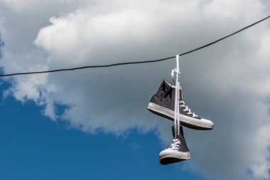 Elektrik kablolarında asılı spor ayakkabıları mavi gökyüzü ve beyaz bulutların arka planında.