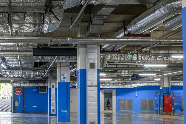 Underground parking of a commercial building. Air ducts of the air conditioning and ventilation system, pipes of the fire extinguishing system, electric cable channels under the ceiling.