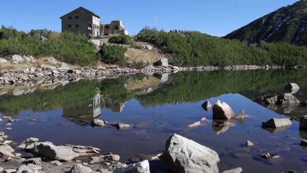 Hombre entrando en la cabaña en el borde del lago de montaña — Vídeos de Stock