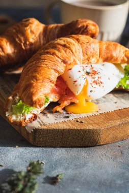 Kavrulmuş yumurta, salata yaprakları, somon ve süzme peynirli kruvasan sandviçi. kahvaltı kavramı