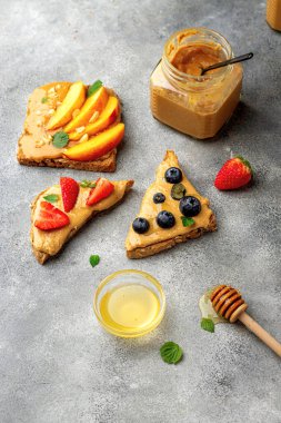 Tam tahıllı tost seti, fıstık ezmesi, bal, nane, fıstık, nektarin, yabanmersini ve çilek. sağlıklı kahvaltı konsepti. fıstık kavanozu