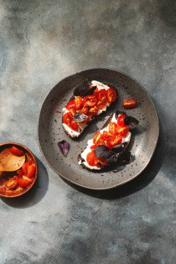 Kiraz domatesli bruschett, süzme peynir, fesleğen, otlar, gri arka planda sarımsak aranıyor. Doğal sert ışık