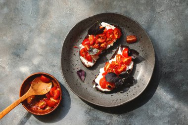 Kiraz domatesli bruschett, süzme peynir, fesleğen, otlar, gri arka planda sarımsak aranıyor. Doğal sert ışık