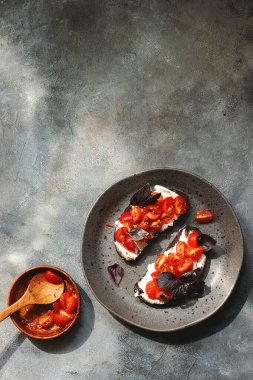 Kiraz domatesli bruschett, süzme peynir, fesleğen, otlar, gri arka planda sarımsak aranıyor. Doğal sert ışık