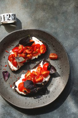 Kiraz domatesli bruschett, süzme peynir, fesleğen, otlar, gri arka planda sarımsak aranıyor. Doğal sert ışık