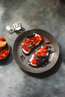Kiraz domatesli bruschett, süzme peynir, fesleğen, otlar, gri arka planda sarımsak aranıyor. Doğal sert ışık