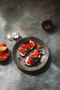 Kiraz domatesli bruschett, süzme peynir, fesleğen, otlar, gri arka planda sarımsak aranıyor. Doğal sert ışık