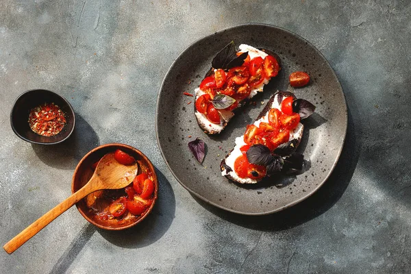 Kiraz domatesli bruschett, süzme peynir, fesleğen, otlar, gri arka planda sarımsak aranıyor. Doğal sert ışık