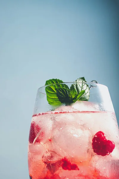 non alcoholic cocktail with raspberry, sparking mineral water, ice cubes, decorated mint leaves on blue background