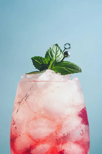 non alcoholic cocktail with raspberry, sparking mineral water, ice cubes, decorated mint leaves on blue background