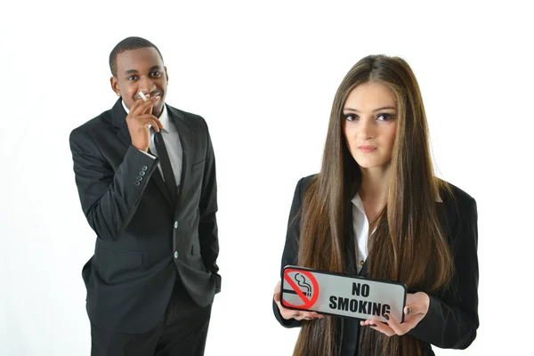 Businesswoman holding No smoking sign  with serious expression and a business man smoking cigarette — Stock Photo, Image