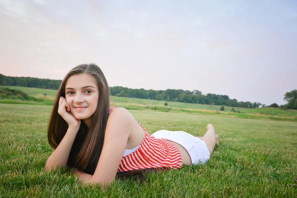 Gelukkige vrouw met hand op kin liggend op gras — Stockfoto