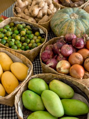 Zencefil, kalamondin, sarı ve yeşil mango, kırmızı ve sarı soğan ve kabak, kurutulmuş palmiye yaprağı sepetlerinde sıralanmış. Küçük bir meyve pazarında satılık..