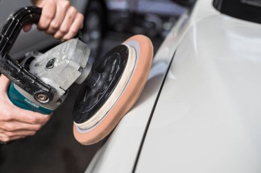 Beyaz bir sedanın kenarını elektrikli cilalama makinesiyle cilalayan bir adam. Bir oto yıkama dükkanında..