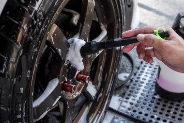 Bir işçi tekerleğin kenarındaki telleri ince bir fırçayla iyice temizler. Tam bir detay ve dış oto yıkama sırasında..