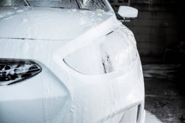 Sabunlar beyaz bir sedanın önüne damlıyor. Kiri ve kiri temizlemek için araba şampuanıyla kaplanmış. Araba yıkama ya da oto yıkama servisinde..