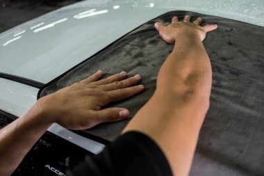 Beyaz bir cipin kaputunu büyük bir mikrofiber havluyla silen bir adam..