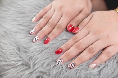 Bitiş jeli olan iki el, gri sahte kürk arka planına karşı karışık tasarımların cilalanmış tırnakları..