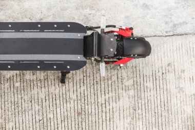 Beton yolun kenarına park edilmiş elektrikli bir scooter 'ın üst görüntüsü. Güverteye ve arka tekere odaklan..
