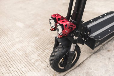 Beton asfalt yolun kenarına park edilmiş elektrikli bir scooter. Ön tekerleğe ve LED farlarına odaklan..