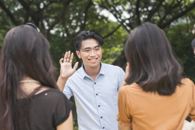 A confident young Filipino man introduces himself to two women. Outdoor scene.