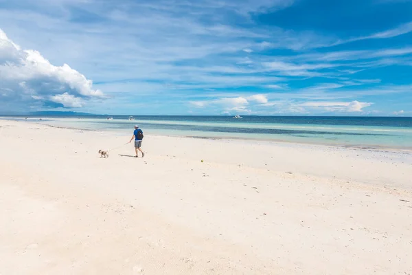 男は自然のままの海岸線と細かい白い砂によって彼の小さな犬を歩く ボホールのパングラオにあるデュマランビーチで ローアングルショット ストックフォト