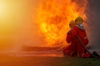 Two firefighters are wearing a fire suit and helmet is extinguishing that the fire is burning