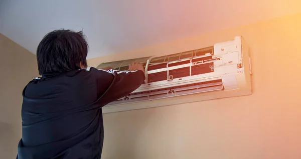 A man is cleaning air conditioner and fixing it on the orange background shade light.