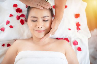 A professional  hand masseuse  massage face for a lady. She is lying on massage table and relaxing, around with rose petals