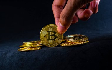 Golden bitcoin, Hand  hold bitcoin at a middle of pile with Black background with ray of light.