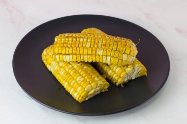 Beyaz arka planda siyah bir tabakta lezzetli ızgara mısır koçanları.
