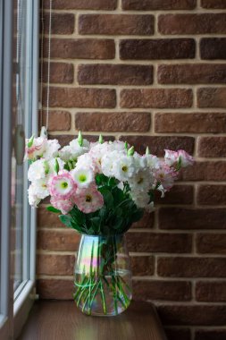 Kahverengi bir pencere pervazında, bir vazoda, tuğla bir duvarın arka planında Eustomas.